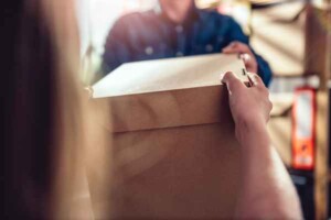 Men,Wearing,Blue,Jean,Shirt,Receiving,Package,From,Courier,At A close-up of two people exchanging a cardboard box, symbolizing delivery or moving. One hand receives it while the other hands it over, creating a feeling of cooperation.